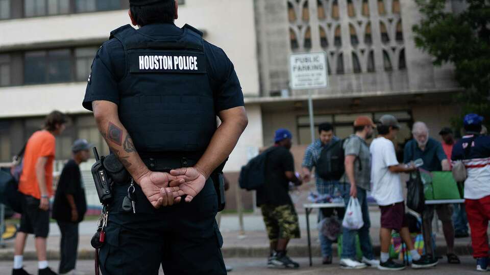 A Houston Police offier watches as volunteers pass out food and supplies outside near he Houston Municipal Court where Bread of Life used to distribute food on Wednesday, Sept. 18, 2024 in Houston. on Wednesday, Sept. 18, 2024 in Houston.