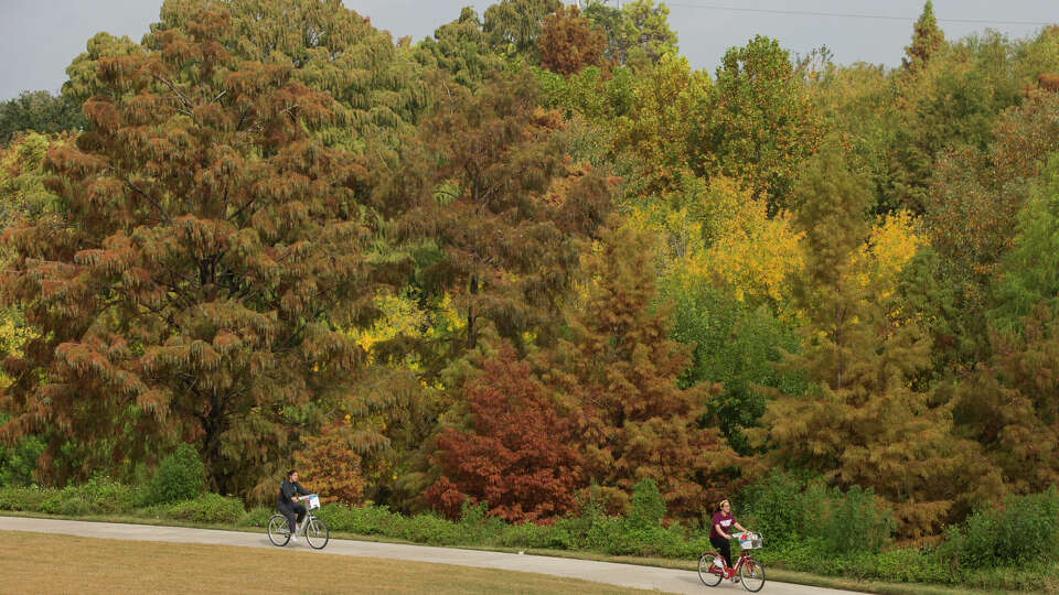 Two cyclists bike past colorful trees on the Buffalo Bayou trails in Houston.