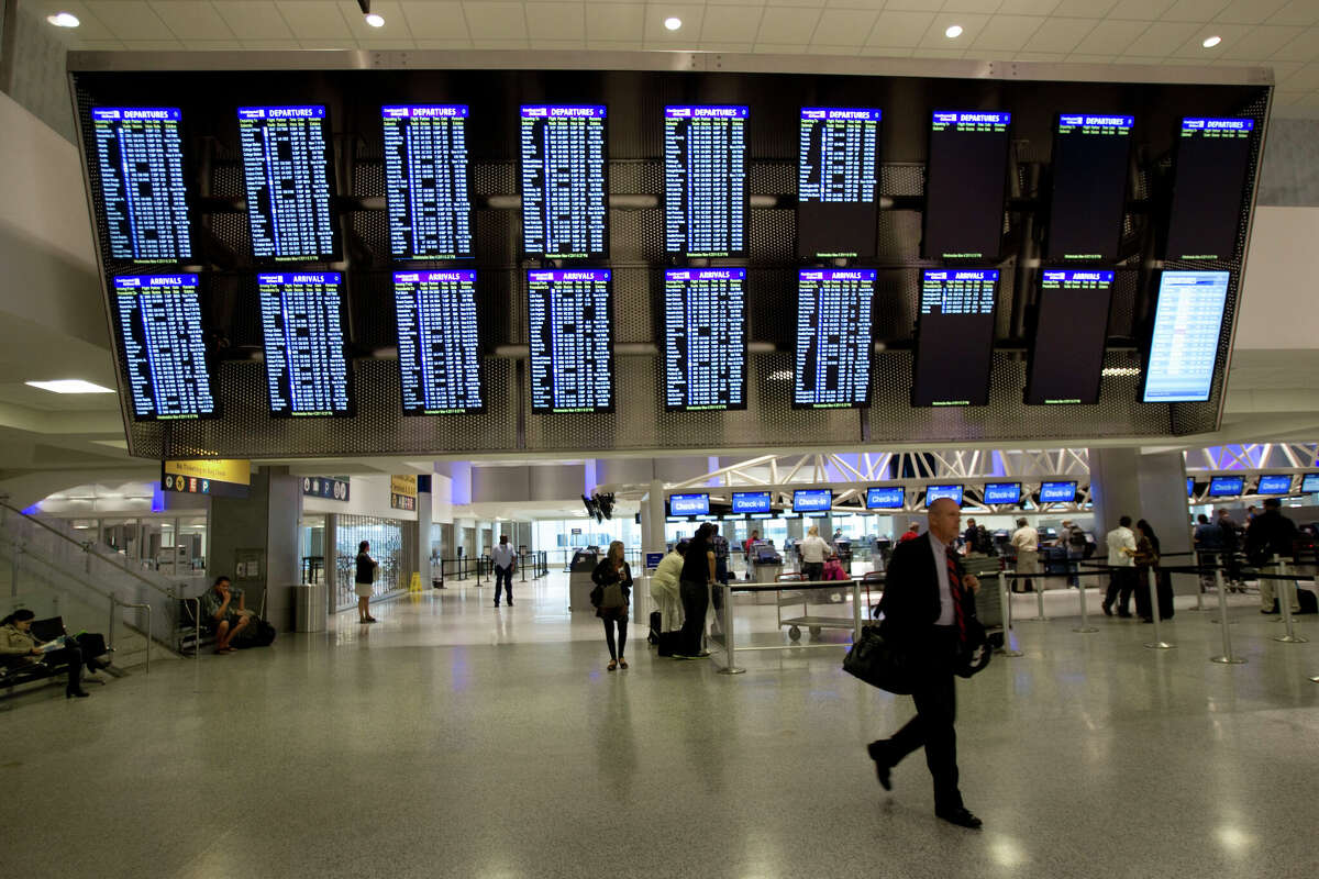 An airline passenger walks under a flight information board at George Bush Intercontinental Airport Wednesday.