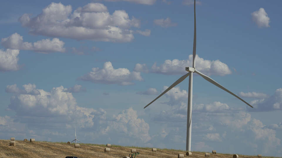 Wind turbines producing energy behind a field of hay barrels Tuesday, Aug. 9, 2022, in Mart.