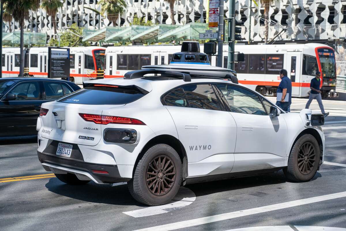 A Waymo vehicle is shown on a busy street with a Muni train in the background in San Francisco, California on August 20, 2024. 