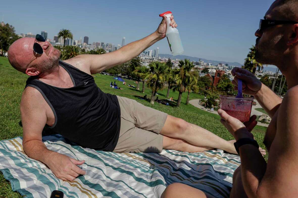 Rob Guzman mists his face with water while sunning in Dolores Park with Ryan Neal in San Francisco on Tuesday, Oct. 1, 2024. It’s officially the city’s hottest day as temperatures creep up toward 100 degrees.