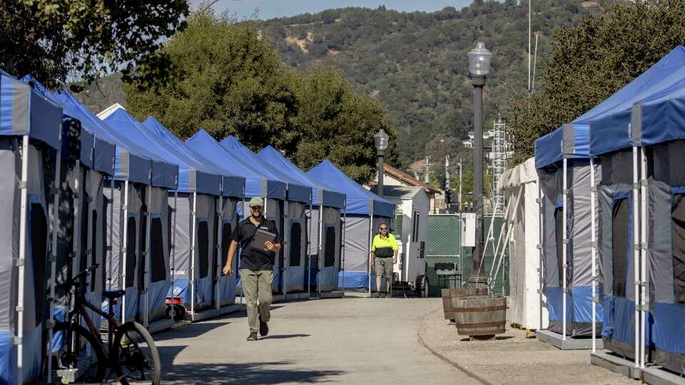 Workers walk between rows of tents at a newly-opened and sanctioned homeless camping site along Lincoln Avenue in San Rafael, Calif., Tuesday, Oct. 8, 2024.