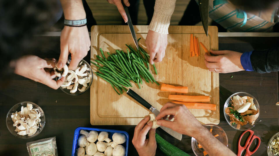 Close up of hands cutting vegetables on a wooden board in cooking class. Food like beans, carrots and mushrooms are getting ready to be cooked on a kitchen desk.