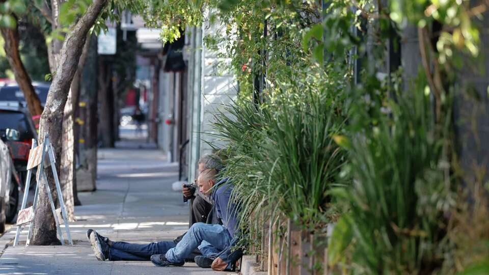 Two people rest against the fence of the Howard Langton Community Garden as they sit on Langton Street on Friday, September 13, 2024 in San Francisco, Calif.