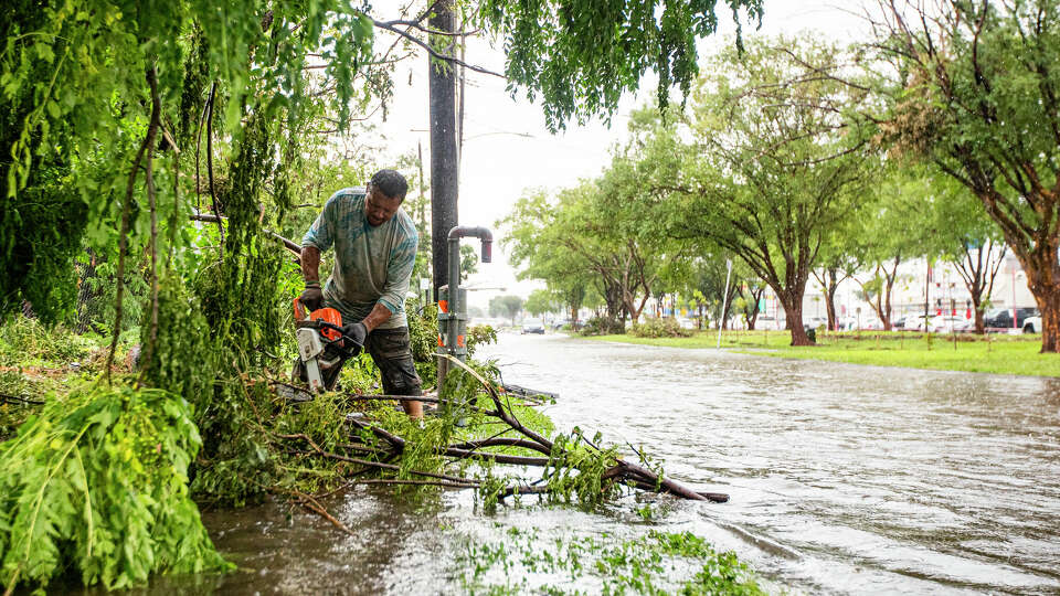 People cut trees that blew over during Beryl as another storm floods the road 5 days after, Thursday, July 11, 2024, in Houston. 