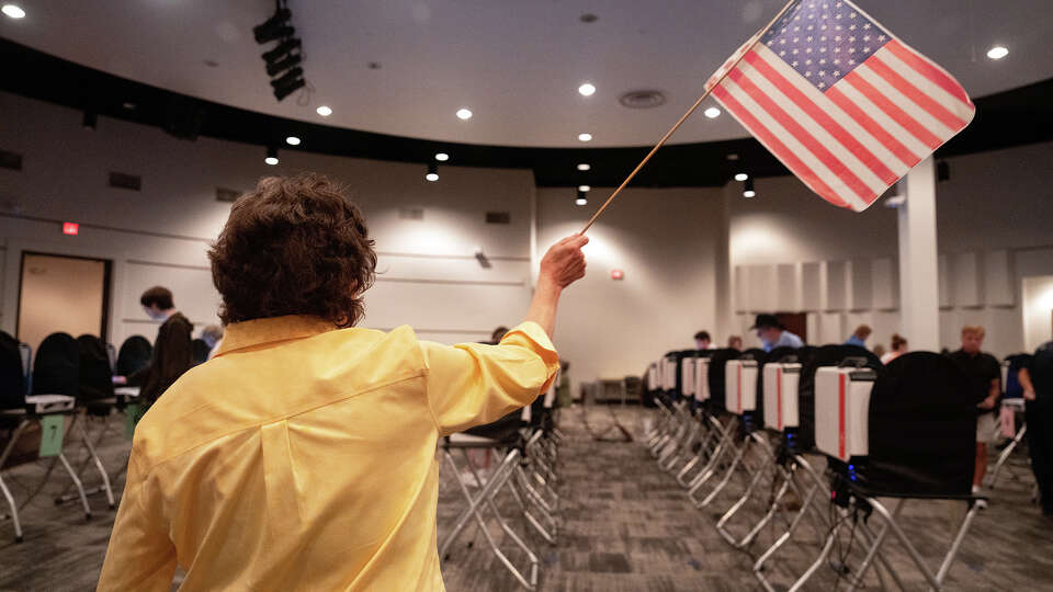 An election clerk waves a U.S. flag to alert voters to the location of the ballot drop off at a polling location at Houston Community College in Houston, TX on October 24, 2024.