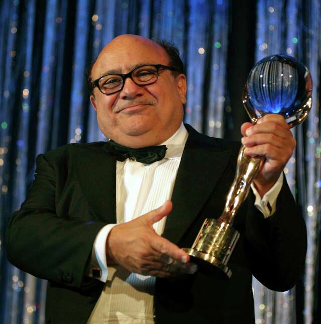 Man in a tuxedo holding a shiny blue and gold award.