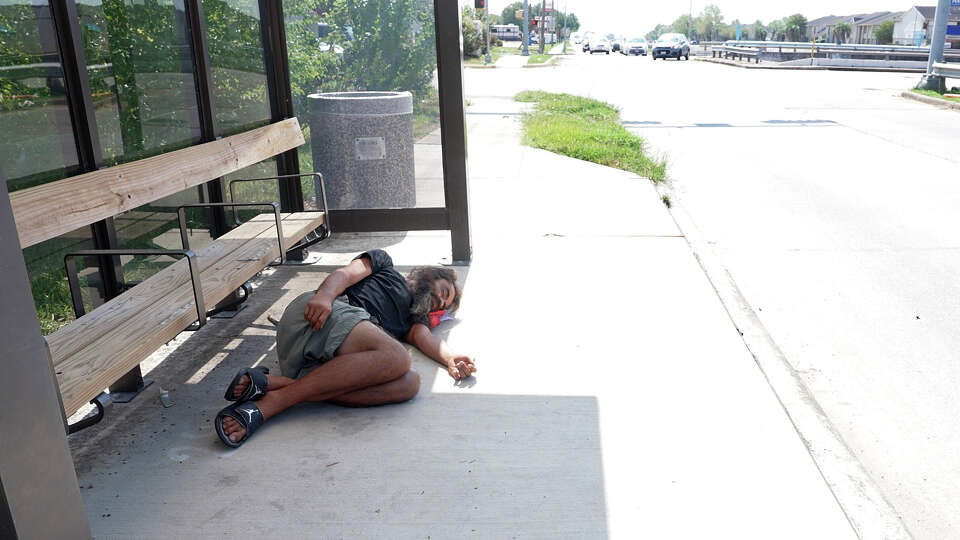 A homeless man sleeps at a bus stop while Sheri Macek makes her way home from Bible study at Sagemont Church in far southeast Houston on September 17, 2023.