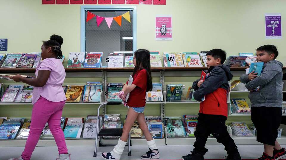 Second grade students line up after selecting books to check out in the library at Burnett Elementary School in Pasadena ISD on Wednesday, Nov. 20, 2024 in Houston. Pasadena ISD is modernizing their reading standards to include more of the science of reading in earlier grades. The schools are also partnering with CYCLE, a nonprofit that gives students free bikes if they reach their academic goals.