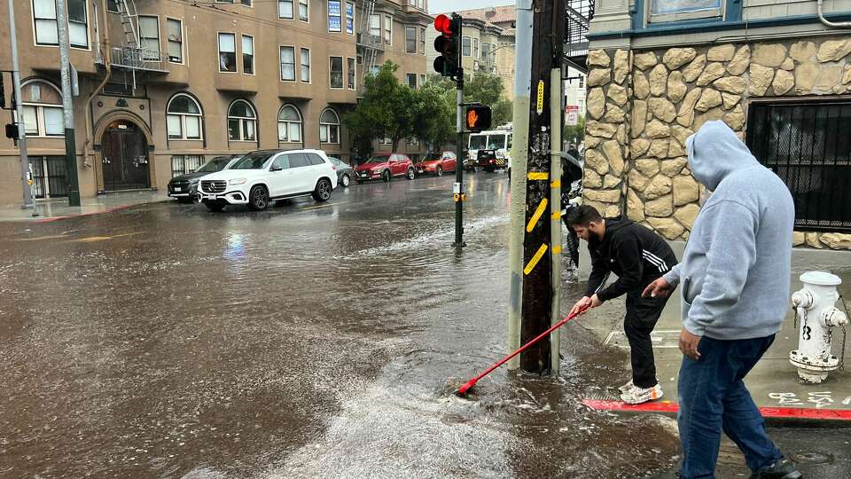 People work to clear a drain on Haight Street as heavy rain comes down in San Francisco on Friday, Nov. 22, 2024.