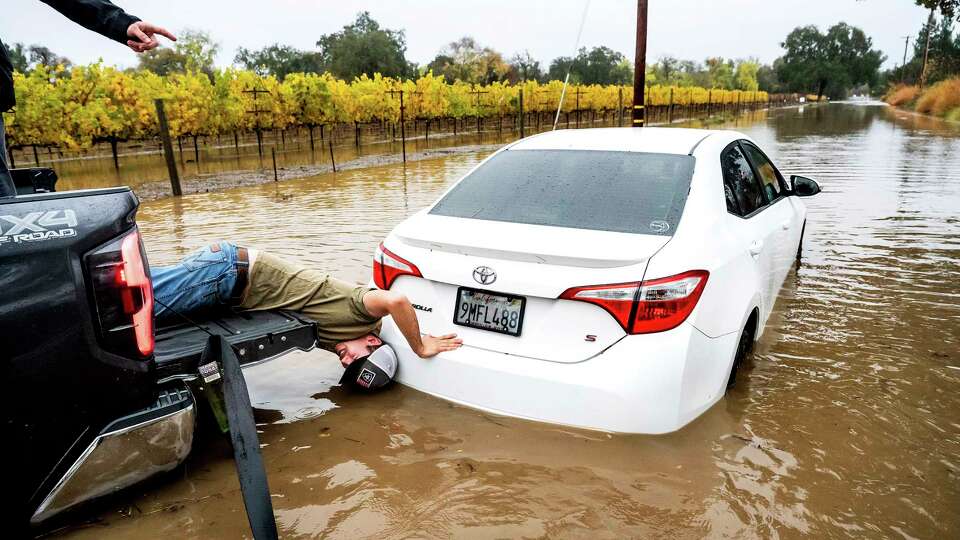 Gabe Sitton works to rescue a driver stuck in floodwaters on Slusser Rd. as heavy rains fall in Windsor, Calif., on Friday, Nov. 22, 2024. (AP Photo/Noah Berger)