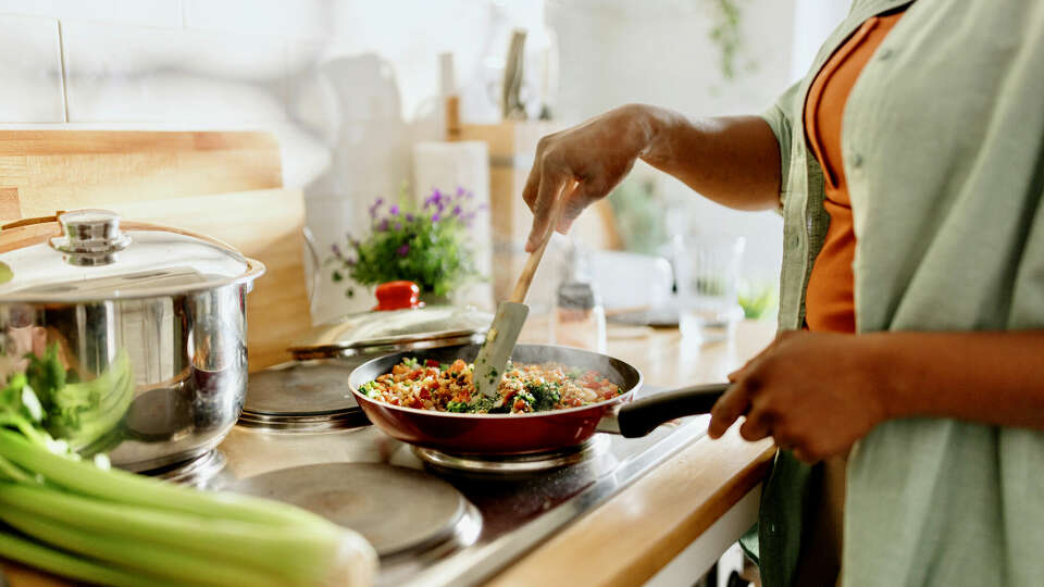 Woman cooking a colourful and nutritious quinoa stir-fry with mixed vegetables and a drizzle of olive oil.