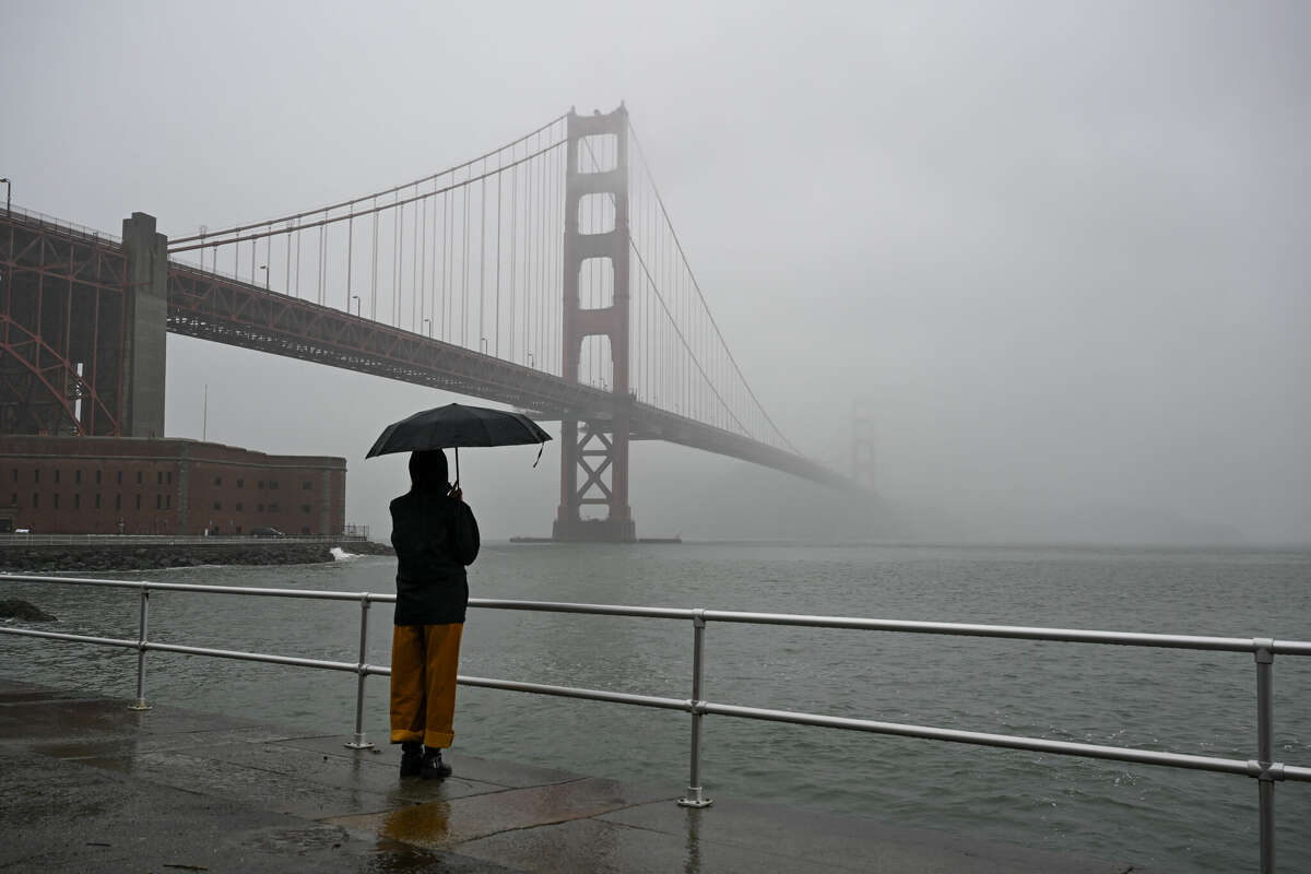 A woman with an umbrella stands near Golden Gate Bridge at Fort Point during rainy weather in San Francisco, California on December 16, 2024.