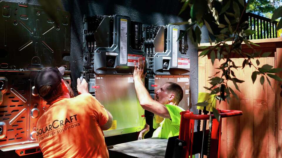 Andrew Magee, right, and Jon Hann with SolarCraft work to install batteries that connect to rooftop solar panels on a home in San Anselmo, Calif. Thursday, Aug. 15, 2024.