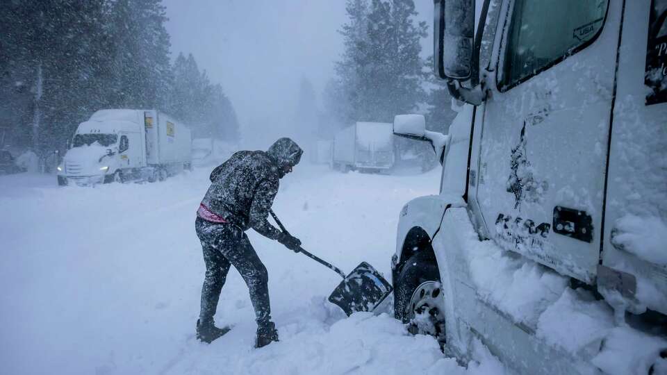 Truckdriver Harry Singh of Seattle tries to dig out some snow to free up his big rig after being stuck overnight in Weed, Calif., on Wednesday, November 20, 2024. The area is getting hit by significant weather throughout the week due to a bomb cyclone off the coast.