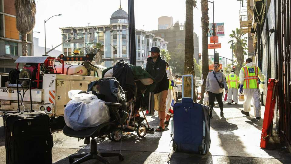 The Department of Public Works cleans the streets as a homeless man named Justin (center) moves his belongings during a sweep on 6th Street in San Francisco on Monday, Oct. 14, 2024.