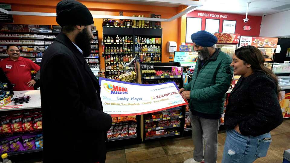 Ishar Gill, left, his father Jaspal Singh, center and his sister Jaspeet Gill right, look over the enlarged image of a check, Saturday, Dec. 28, 2024, that will be presented to the winner of $1.22 billion Mega Millions Lotto ticket that was purchased at their family's store in Cottonwood, Calif., Saturday, Dec. 28, 2024. (AP Photo/Rich Pedroncelli).