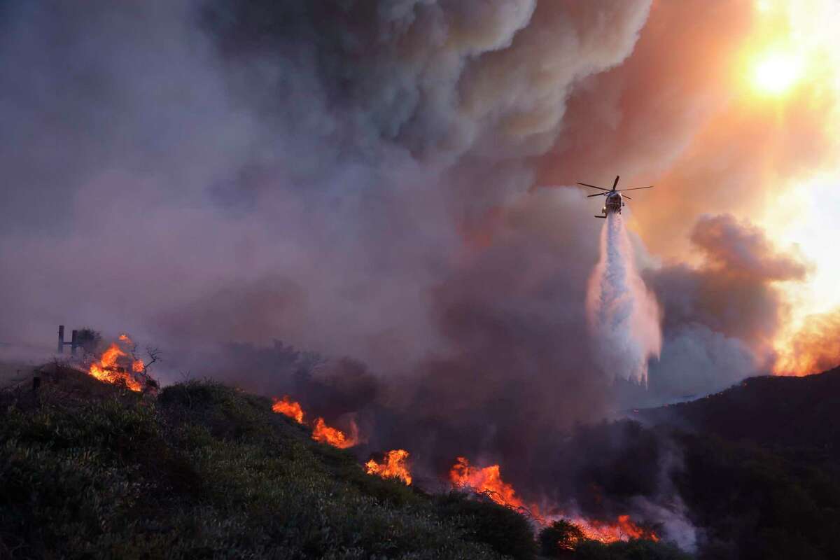 Water is dropped by helicopter on the advancing Palisades Fire in the Pacific Palisades neighborhood of Los Angeles, Tuesday, Jan. 7, 2025.