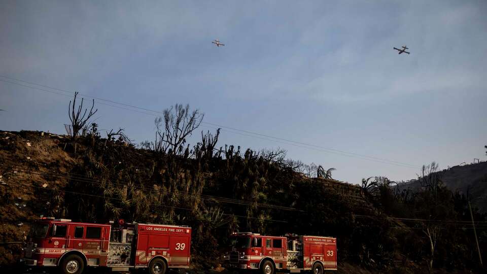 Two firefighting aircraft fly overhead during the Palisades Fire in Pacific Palisades, Calif., Thursday, Jan. 9, 2025.