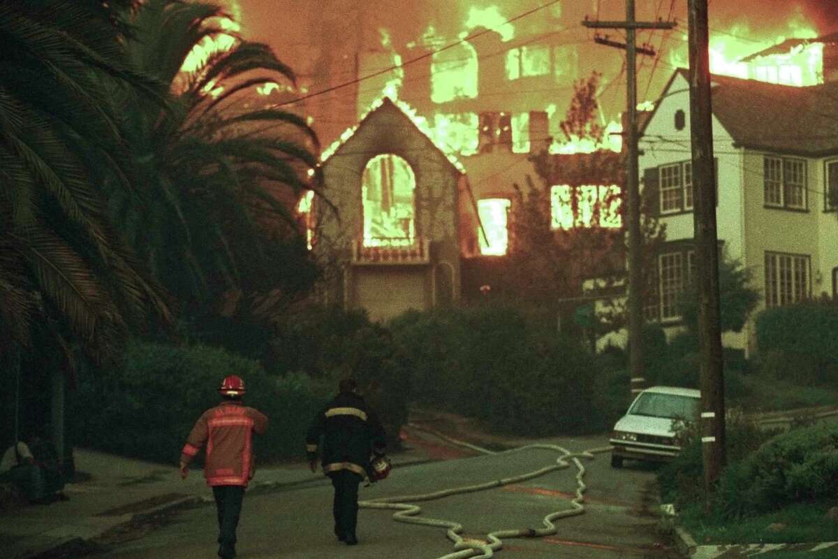 Firefighters walk up Rockridge Blvd. towards burning homes in Oakland, Calif., Oct. 20, 1991. A wind-driven brush fire exploded into a firestorm Sunday as it roared through upscale residential neighborhoods in the hills above Oakland, engulfing hundreds of homes and killing five people, authorities said. (AP Photo/Olga Shalygin)