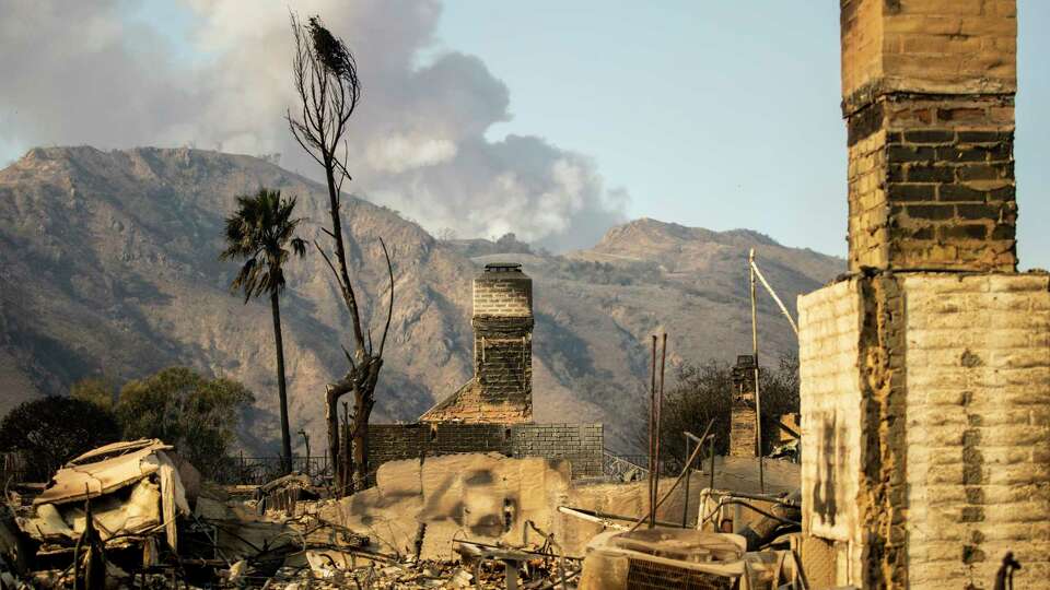 Homes destroyed by the Palisades Fire are seen as a smoke column rises in the distance in Pacific Palisades, Calif., Friday, Jan. 10, 2025.