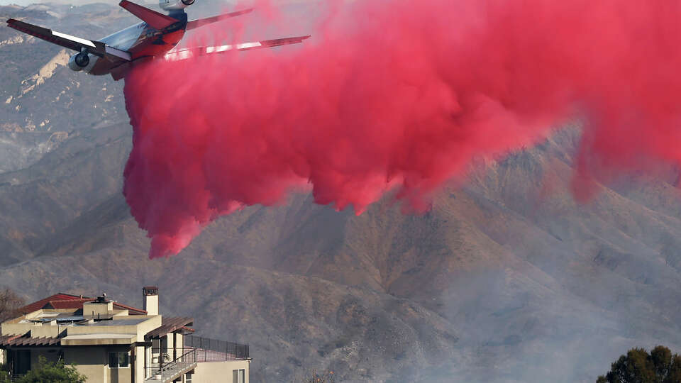 TOPANGA, CALIFORNIA - JANUARY 10: A person (BOTTOM) watches from a balcony as a firefighting aircraft drops the fire retardant Phos-Chek near homes during the Palisades Fire as wildfires cause damage and loss through Los Angeles County on January 10, 2025 in Topanga, California. Multiple wildfires fueled by intense Santa Ana Winds are burning across Los Angeles County. Reportedly at least 10 people have died with over 180,000 people having been under evacuation orders. Over 9,000 structures have been damaged or burned while more than more than 25,000 acres were burning from the fires. (Photo by Mario Tama/Getty Images)