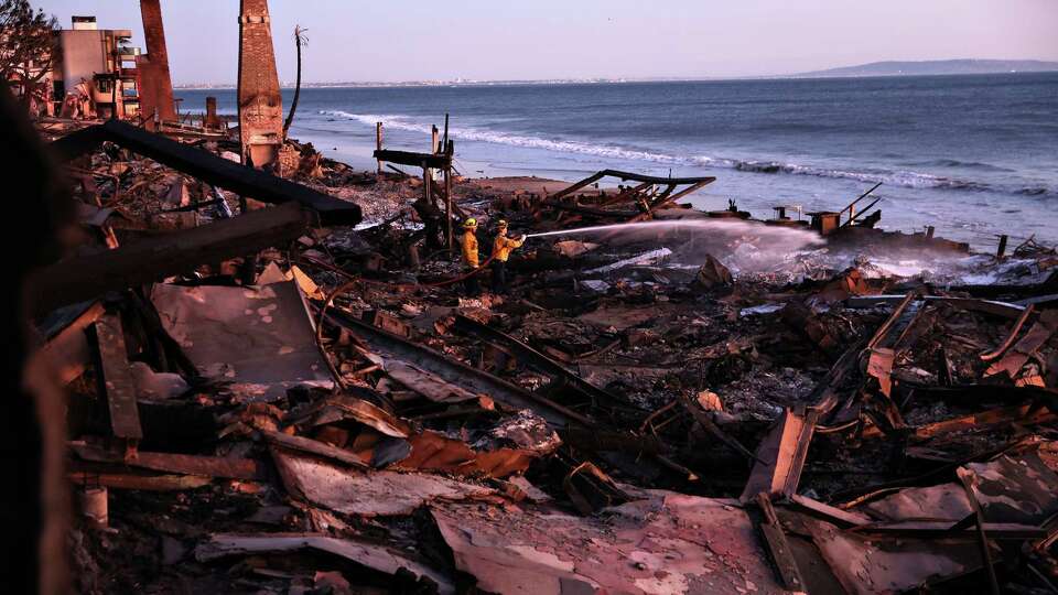 Los Angeles Fire Department’s Dylan Casey and Mike Alvarez work on extinguishing a hot spot during aftermath of Palisades Fire along Pacific Coast Highway in Malibu, California on Sunday, January 12, 2025.