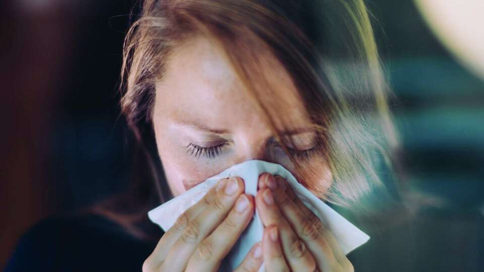 A woman sneezes behind a window, using a tissue. For her latest column, Vanessa Hua writes about catching her first cold since returning to social life as pandemic restrictions loosen in California.