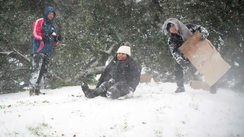 Marleen Martinez, center, with an assist from Vincent Tran, tries to sled down a hill in Buffalo Bayou Park on Tues. Jan. 21, 2025 in Houston. Looking on is John Neal, left.