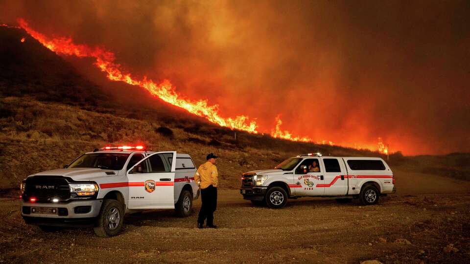 Firefighters monitor flames caused by the Hughes Fire along a roadside in Castaic, Calf., Wednesday, Jan. 22, 2025. (AP Photo/Ethan Swope)