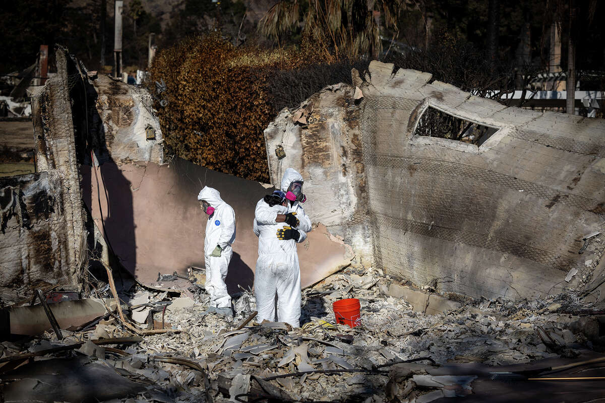 Wearing protective gear, Eaton fire victims and neighbors Kara Marsh hugs Ian Crick and as his friend Matt Listiak helps Crick search for keepsakes and valuables at his burned out home of 3.5 years on W. Marigold Street, as residents return to their burned out homes in Altadena Tuesday, Jan. 21, 2025.