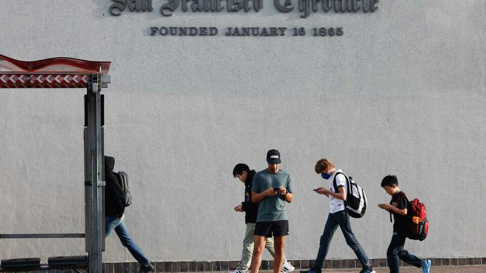 Pedestrians walk past San Francisco Chronicle signage as others wait at a bus stop on Friday, January 24, 2025 in San Francisco, Calif.