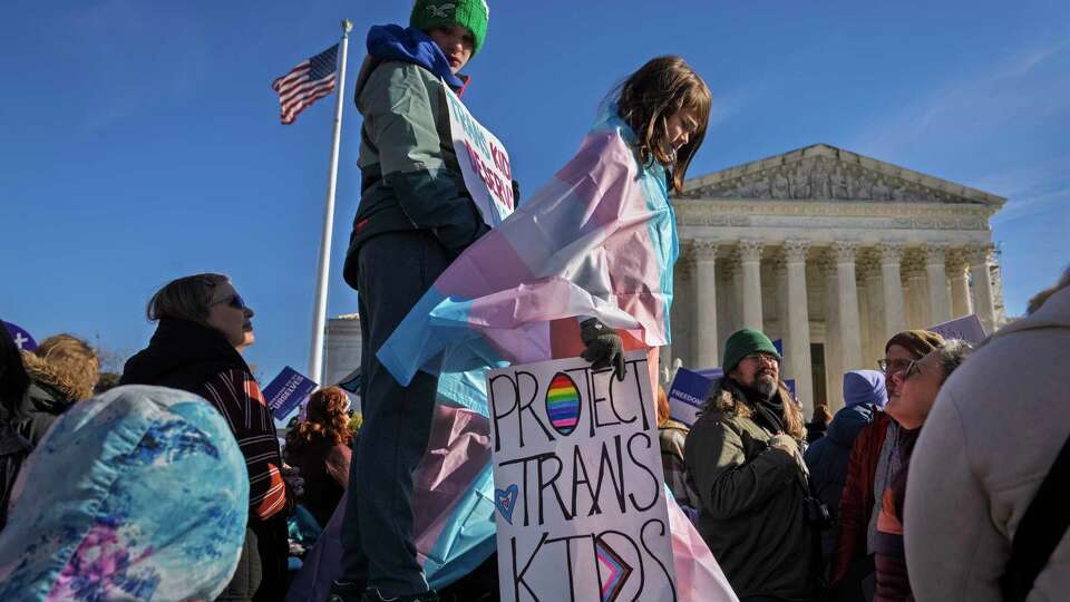 FILE - Nate, 14, left, and Bird, 9, right, hold signs and transgender pride flags as supporters rally outside the Supreme Court, Dec. 4, 2024, in Washington, while arguments are underway in a case regarding a Tennessee law banning gender-affirming medical care for transgender youth. (AP Photo/Jacquelyn Martin, File)