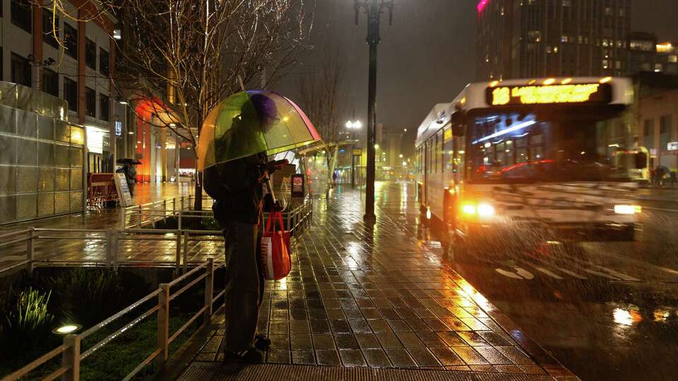 A person with a rainbow umbrella waits for the bus on Shattuck Avenue in Berkeley, Calif., as rain falls on Saturday, Feb. 1, 2025.