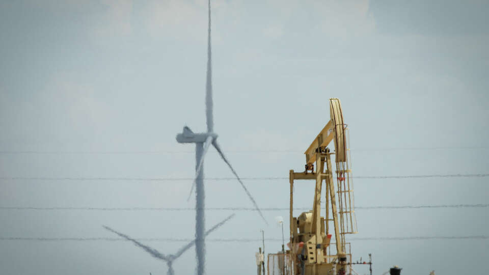 A pumpjack is obscured by the heat as it operates on dry farmland with large windmills Friday, July 8, 2022, near Midland.