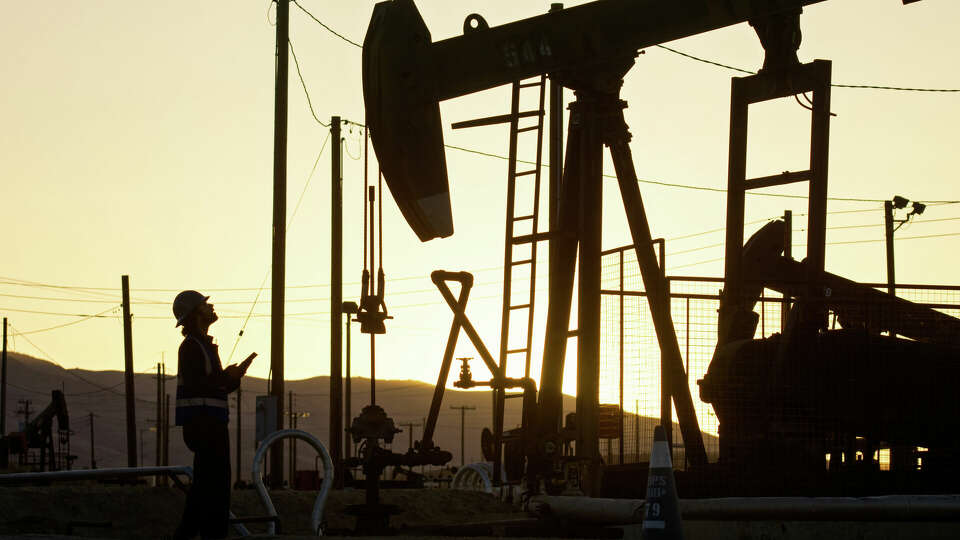 An Indian oilfield worker facing an oil pump jack at sunset in Kern County, California.
