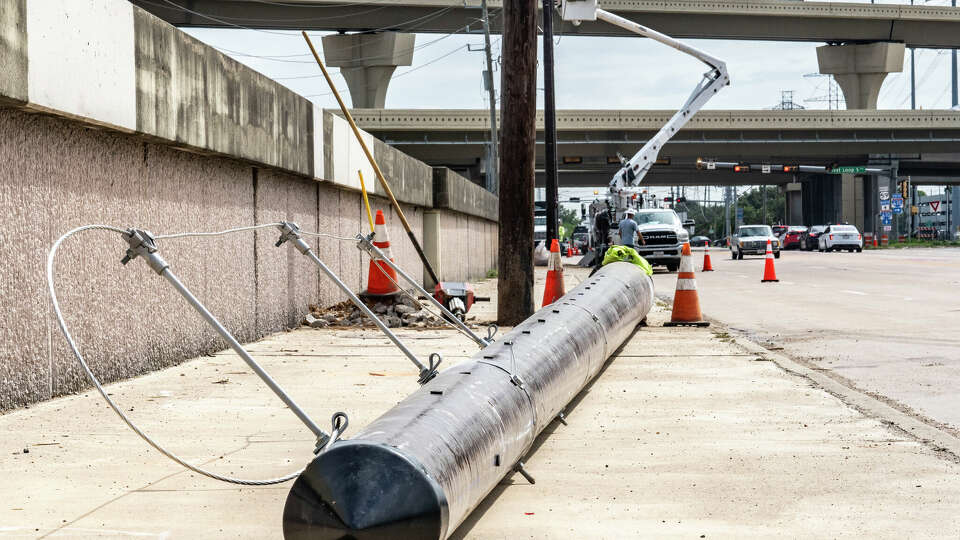 A modern metal power pole lies in the foreground as a utility line crew works to replace older wooden poles with a modern metal poles along Westpark Drive near the IH-610 interchange Tuesday, Sep 10, 2024 in Houston.
