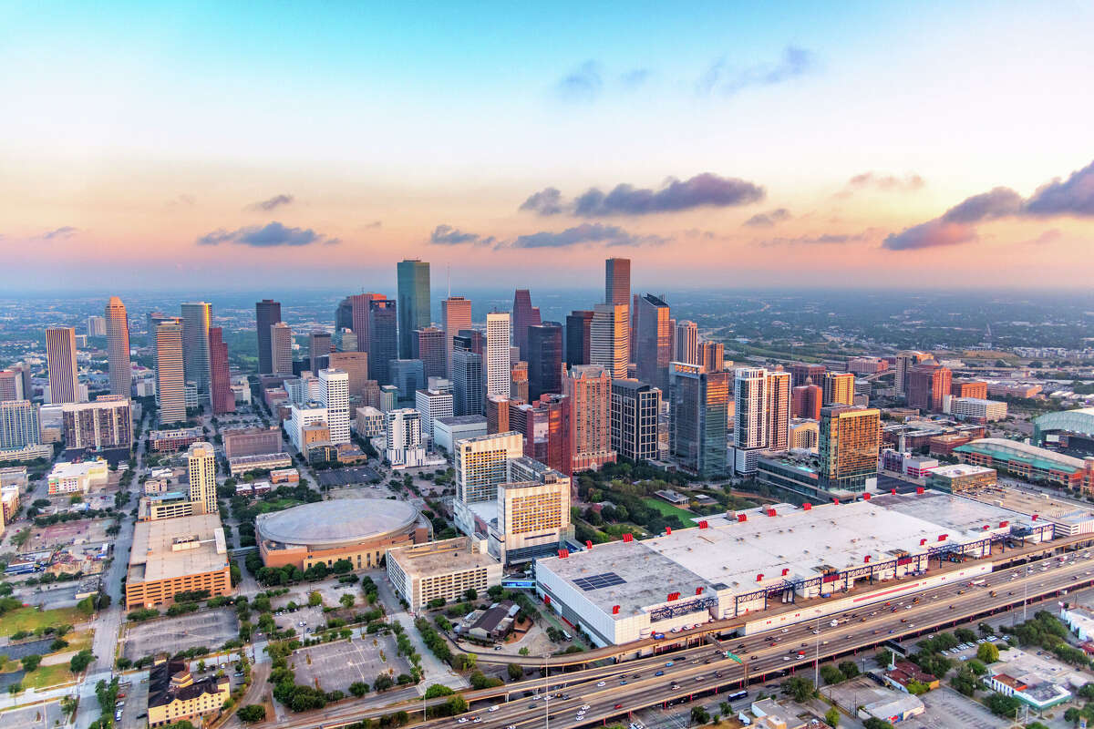 The skyline of Houston, Texas shot at daybreak from a helicopter at an altitude of about 700 feet over the east side of downtown with Toyota Center, George R. Brown Convention Center, and Daikin Park in the foreground.