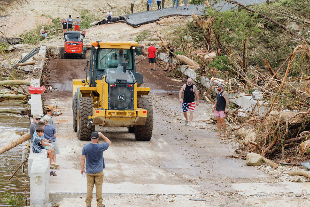 Humble resident, Darren Urie, center and wearing American flag shorts, crosses the Cade Loop bridge with his cousin as work crews clear and temporarily repair a bridge connecting Texas 39 to a residential area over the Guadalupe River in Ingram on Saturday July 5, 2025.