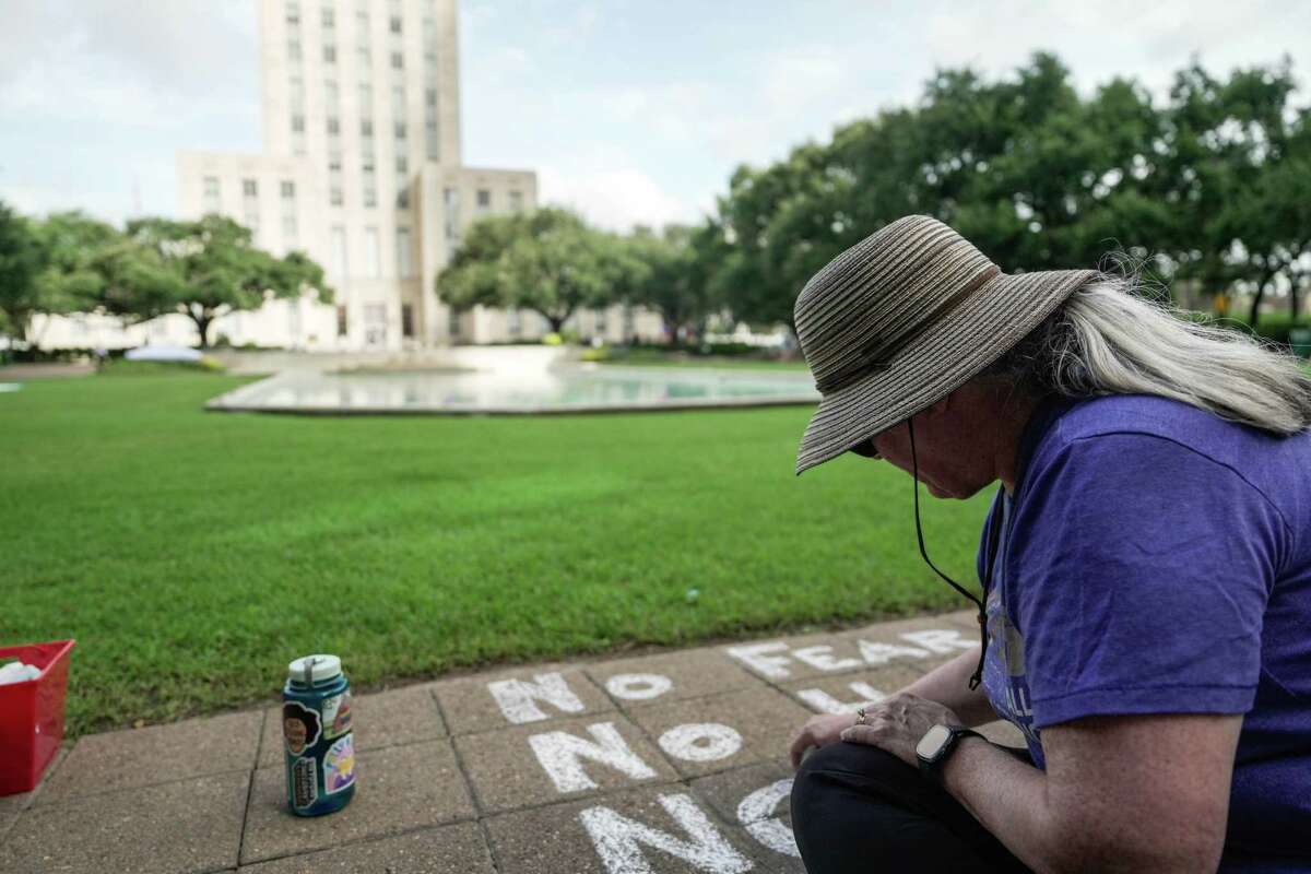 A woman writes in chalk at a nationwide protest, Good Trouble Lives On, in front of City Hall on Thursday, July 17, 2025 in Houston.