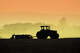 Muted backlit silhouette of two tractors raking soil in California’s San Joaquin Valley.