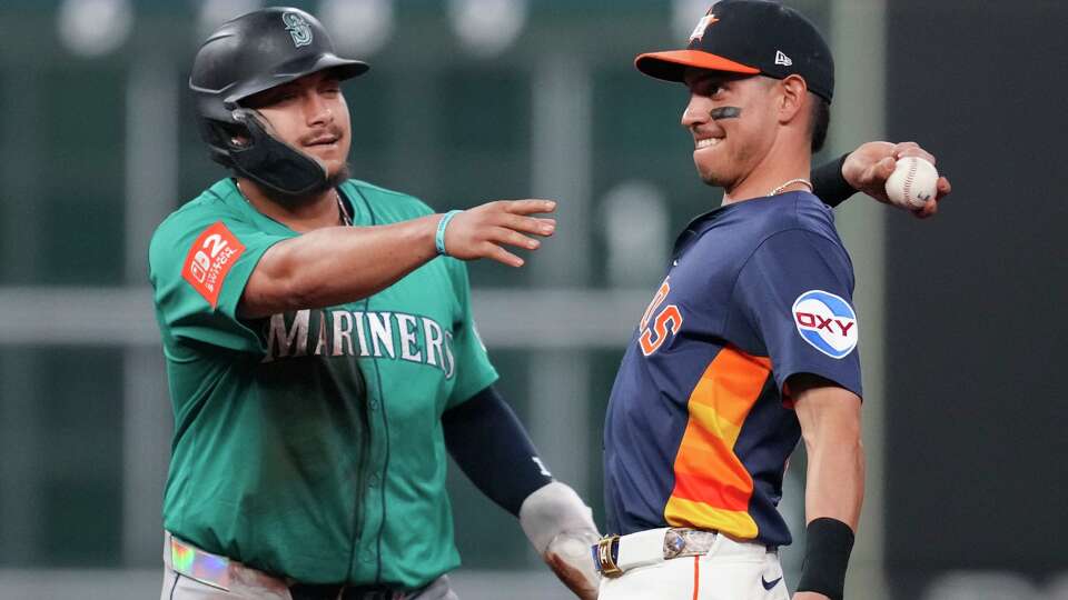 Seattle Mariners Josh Naylor (12) tries to mess with a throw by Houston Astros shortstop Mauricio Dubón (14) back to catcher Yainer Diaz after Dubón tried to fake Naylor out to step off the bag during the eighth inning of a MLB baseball game in Houston, Sunday, Sept. 21, 2025.