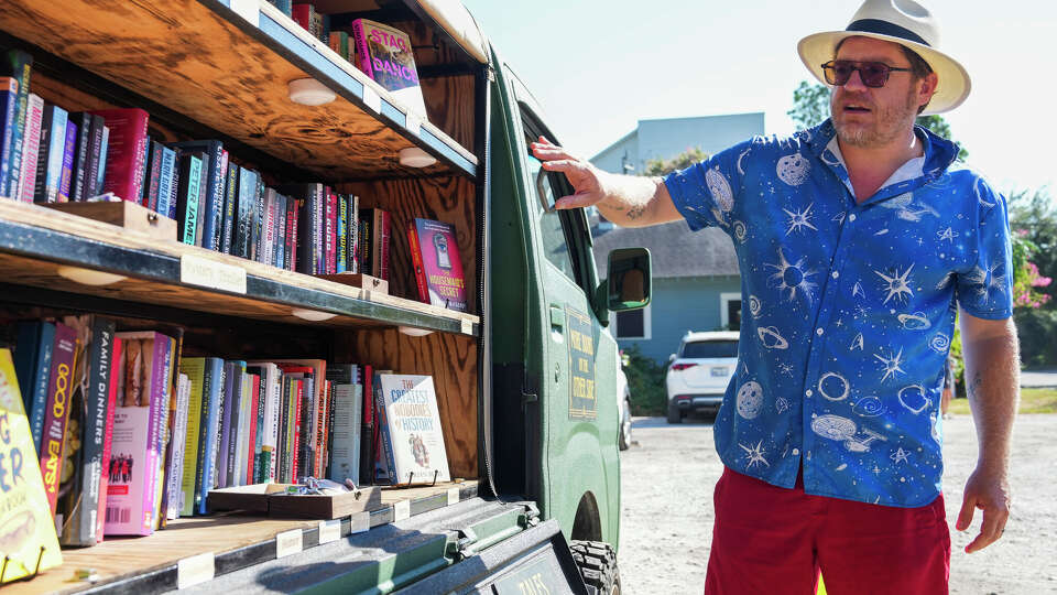 Brian Wilson helps a customer choose a book at Wilson Mobile Books outside Chilosos Taco House in Houston, Sunday, Oct. 12, 2025.