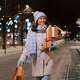 Woman wearing a white coat with blue winter hat and scarf wallking on a downtown street carrying holiday gift boxes.