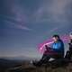 Couple using their model phones with sitting on a mountain in the moonlight
