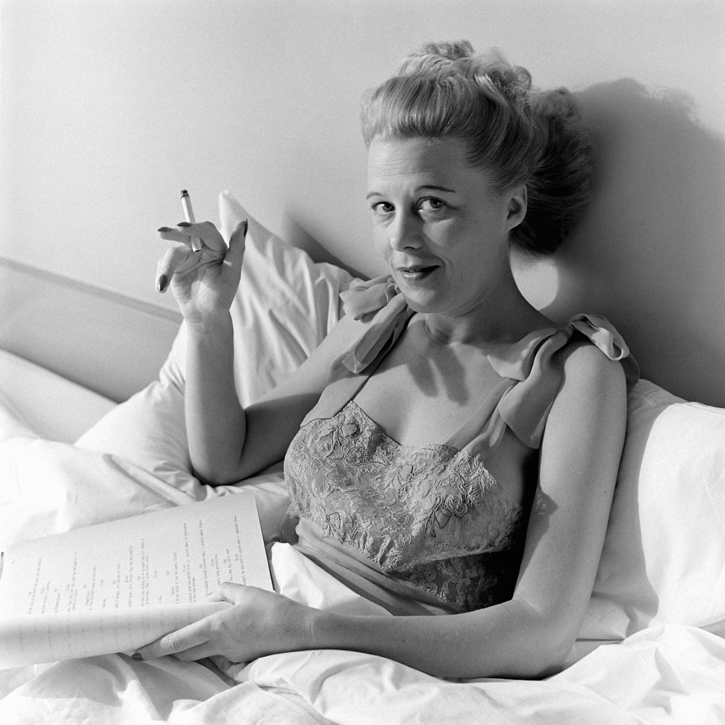 Joan Harrison, screenwriter and producer smoking and reading a script in bed at her home in Los Angeles, 1945