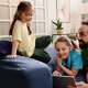 A dad and his two daughters lay on a couch, looking at their tablet