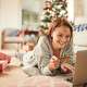 Woman laying on the floor in her festive living room using her laptop to shop for the holidays.
