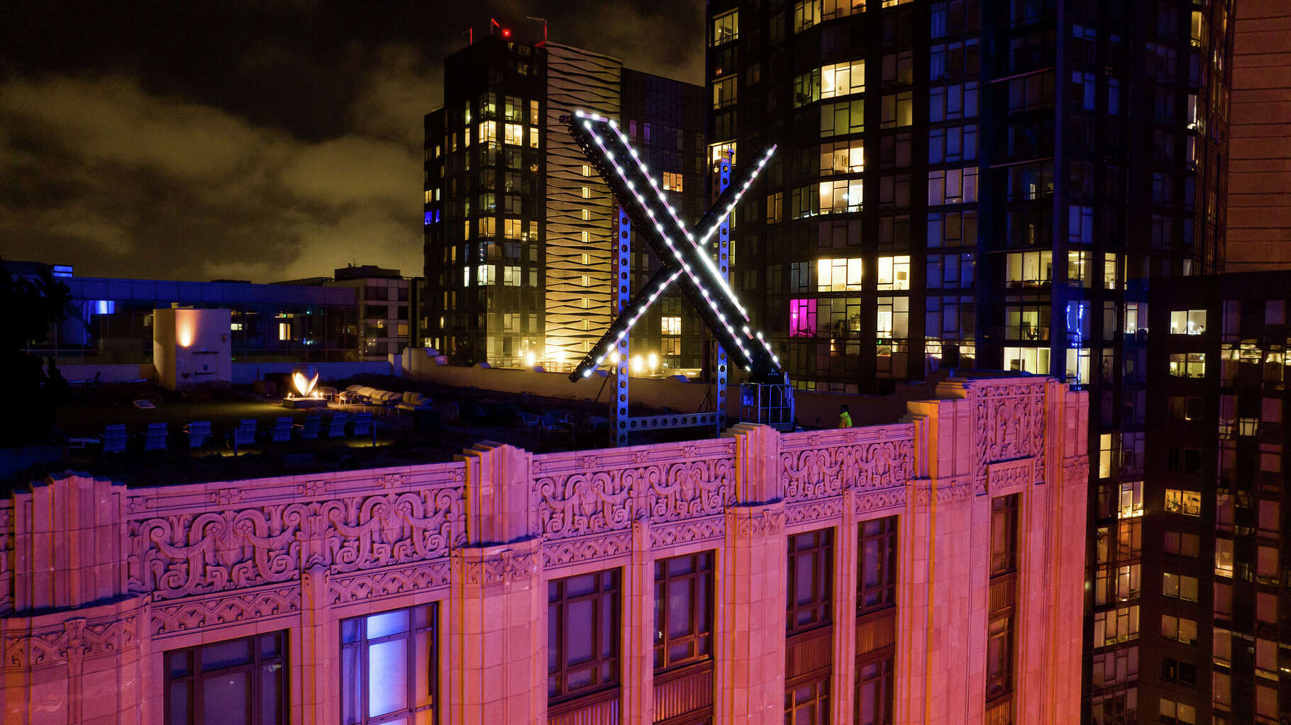 Workers install lighting in fall 2023 on an 'X' sign atop the former company headquarters in downtown San Francisco. The company's headquarters later moved to Bastrop.